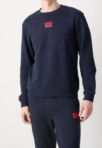 Felpa blu navy realizzata in morbido tessuto, con un patch rettangolare rosso sul petto e polsini e orlo a costine.