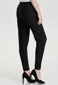 Zwarte pinstripe broek met een slim fit, voorzien van achterzakken en een gladde textuur, gecombineerd met zwarte hoge hakken.