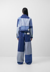 Jeansjacka och vida byxor i olika nyanser av blått, med ett lapptäcksmönster och en avslappnad passform med synliga sömmar.