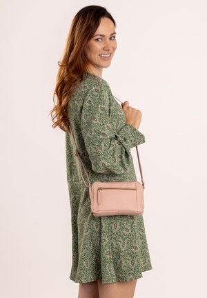 Hellrosa Leder-Crossbody-Tasche mit einem Reißverschlussfach, rechteckiger Form und einem langen verstellbaren Trageriemen, präsentiert vor einem neutralen Hintergrund.