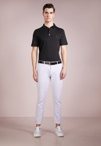 Svart kortermet polo skjorte, hvite slim-fit bukser, svart belte og hvite joggesko. Glatt stoff, klassisk krage og avslappet passform.
