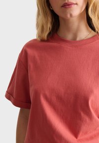 Röd bomullströja med korta ärmar och rund halsringning, med en mjuk textur och minimalistisk design. Inga synliga logotyper eller mönster.