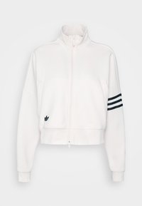 Valkoinen vetoketjullinen huppari, jossa on korkea kaulus, ribattuja hihansuita ja musta kolmonauhatyyli hihassa. Edessä pieni musta logo.