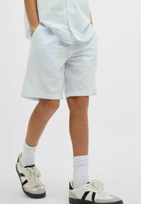 Shorts à motifs bleu clair en tissu texturé, avec des poches latérales, accompagnés de chaussettes blanches et de baskets à accents noirs.