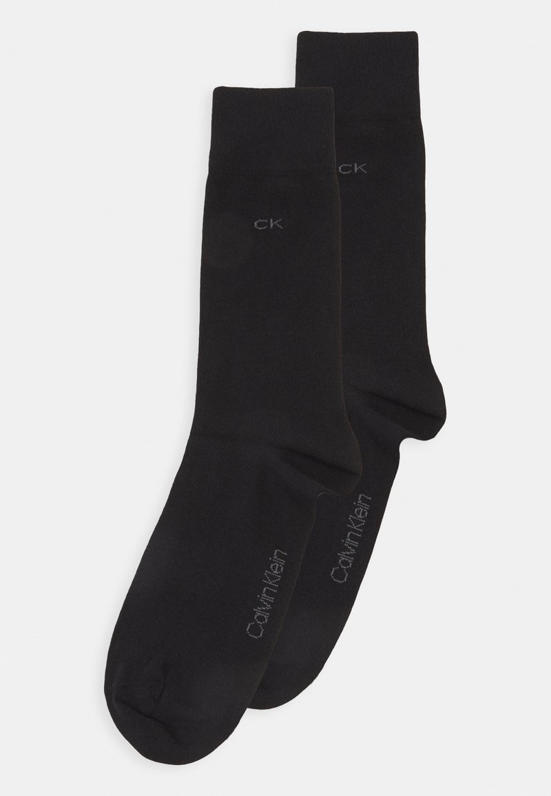 Calcetines de algodón negros con textura acanalada, que presentan la marca Calvin Klein en gris a lo largo del costado. Longitud estándar de tipo crew y diseño de punta sin costuras.