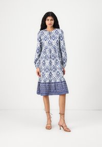 Rochie cu mâneci lungi, de lungime până la genunchi, având un model floral alb și albastru, guler rotund și margine evazată. Asortată cu sandale cu barete.