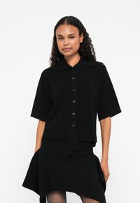 Μαύρη ριγωτή πλεκτή μπλούζα με κοντά μανίκια, γιακά και κουμπί κλεισίματος. Διαθέτει άνετη εφαρμογή και υφή μαλακού υφάσματος.