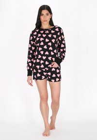 Svarta pyjamaser med kort ärm och shorts, med ett mönster av rosa hjärtan. Mjuk tygkvalitet med avslappnad passform; fållade ärmar och nederkant.