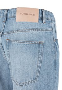 Light blue denim jeans back pocket with brown stitching and tan leather brand label reading "2Y STUDIOS" on waistband.