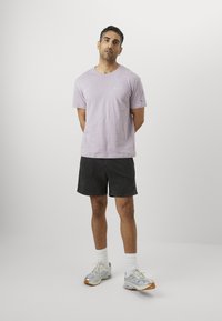 Lavendel bomull t-skjorte med rund hals, sammen med svarte shorts. Har hvite sokker og grå joggesko med oransje detaljer.