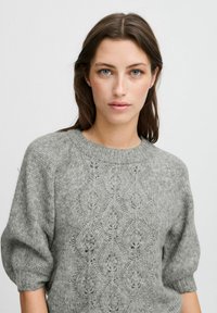 Grauer gestrickter Pullover mit einem runden Halsausschnitt, kurzen puffärmel und einem strukturierten Muster, das durchgängig aus Rautenmuster besteht.