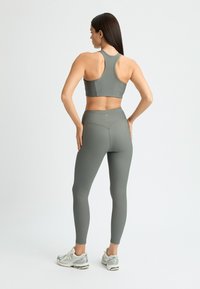 Sport-BH och leggings i ribbat olivgrönt tyg. Har en racerback-design och hög midja. Matchas med silvriga löparskor.