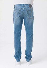 Jeans in denim azzurro chiaro con gambe dritte, tasche standard e un'etichetta sul retro. Il tessuto mostra una leggera scoloritura. Indossati con sneaker bianche.