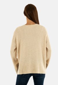 Maglione in maglia beige chiaro con vestibilità ampia, orlo a costine e texture morbida. Presenta un colletto tondo e un design con spalle scese.