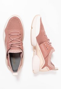 Jasnoróżowe buty sportowe z przewiewną siateczką, teksturowanymi akcentami i masywną białą podeszwą. Posiadają sznurowany zapięcie i pętelkę.