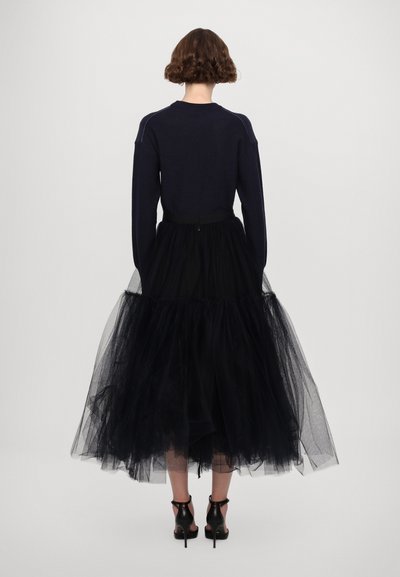 Black tulle skirt with layered texture, paired with a fitted navy sweater. The outfit features a waist belt and black high-heeled shoes.