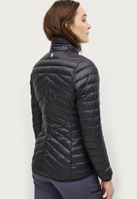 Sort pufferjakke med chevron-quilting, høj krave og et lille logo på ryggen. Dets skinnende materiale tilføjer en elegant tekstur.