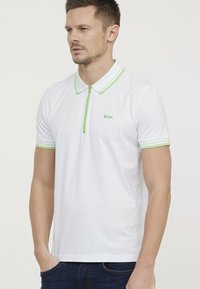 Witte polo met groene accenten op de kraag en mouwen. Heeft een ritssluiting aan de voorkant en een klein logo op de borst.