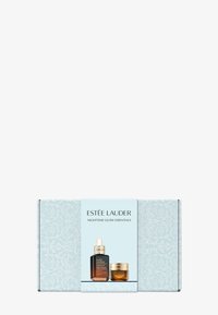 Le set Estée Lauder Nighttime Glow Essentials dans une boîte bleu clair contient une bouteille de sérum sombre et un pot de crème accentué d'or, tous deux étiquetés.