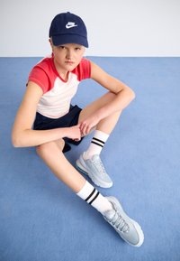 Light blue sneakers with textured mesh and white sole, paired with black and white striped socks. Red and white raglan t-shirt and navy shorts.