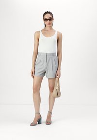 Gray tailored shorts with pleats, worn with a white tank top and teal high-heeled sandals. A beige handbag is held in one hand.