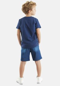 Camiseta de algodón azul marino combinada con pantalones cortos de mezclilla, con un corte relajado y zapatillas blancas con cremallera en la parte trasera.