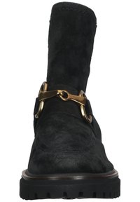 Bota de tornozelo em camurça preta com bico arredondado, uma fivela decorativa em metal dourado e uma sola de borracha texturizada com tração.