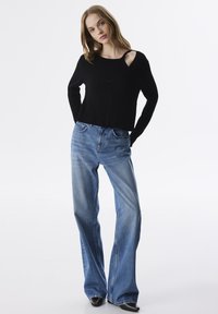 Pull noir à côtes avec un design court et un détail découpé au niveau du col, associé à un jean flare bleu clair et des chaussures noires à bouts pointus.
