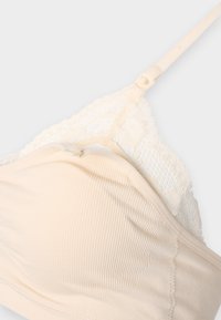 Bralette bege com tecido canelado e acabamento em renda. Apresenta alças ajustáveis e uma textura suave, proporcionando um ajuste confortável e macio.