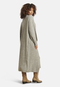 Cardigan lungo grigio lavorato a maglia con motivo a rilievo, polsini a coste e spacchi laterali. Indossato sopra stivali color cuoio alti fino al ginocchio.