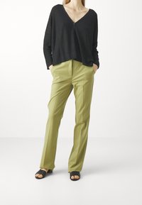 Svart ribbad stickad tröja med v-ringning och knappdetalj, paired med ljus olivgröna skräddarsydda byxor och svarta sandaler med öppen tå.