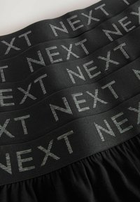 Schwarzes Gummiband mit sich wiederholendem grauem "NEXT"-Text, featuring eine glatte Textur und gerafftem Stoff darunter.