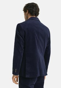 Marineblaue Cord-Blazer mit Revers, mittigem Schlitz und Detail mit vier Knöpfen an den Manschetten. Das strukturierte Gewebe sorgt für visuelle Akzente.