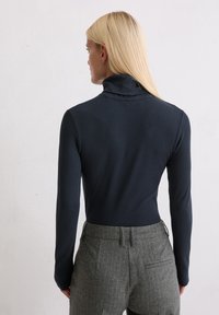 Navy langmouw turtleneck top, aansluitend ontwerp, gemaakt van gladde stof, gecombineerd met grijze, gestreepte tailleurbroek.