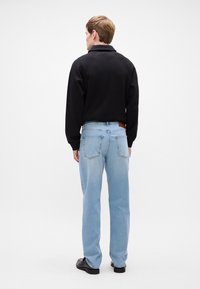 Mustvalgusega must dressipluus koos kraega, mille alla on sobitatud helesinised sirge lõikega teksad. Teksadel on tagataskud ja vöökoht on kaunistatud pruuni nahkpaisuga.