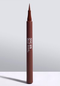 Brun penn eyeliner med fin tupp. Mat overflate på rørformet, merket med "575" og "THE COLOR PEN EYELINER" i hvit tekst.