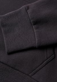Polsini della felpa nera con texture a coste, caratterizzati da un tessuto morbido e un dettaglio della tasca piatta cucita. Dettaglio ravvicinato del materiale e del design.