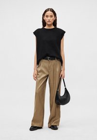 Czarny, oversizowy, dziany top, beżowe spodnie o szerokich nogawkach z paskiem, czarna torba na ramię i czarne mokasyny. Proste, teksturowane tkaniny w neutralnych tonach.