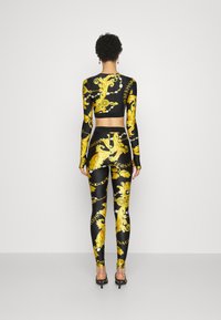 Crni i zlatni komplet s kratkim topom i tajicama s intrikatnim baroknim uzorcima i natpisom, izrađen od rastezljivog materijala, s dugim rukavima.