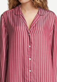 Röd randig button-up skjorta med vita vertikala linjer, med krage och långa ärmar. Materialet verkar lätt och något genomskinligt.