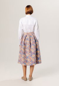 Witte blouse met knopen, gecombineerd met een bloemenpatroon, knielange rok in roze, blauw en crèmekleuren. Simpele bruine ballerinashoes maken de look compleet.