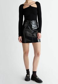 Top nero a maniche lunghe con costine e dettagli cut-out, abbinato a una mini gonna nera in vernice alta in vita con cintura. Mocassini neri completano l'outfit.