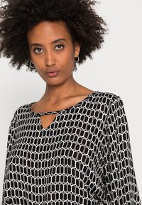 Blusa bianca e nera con un motivo geometrico esagonale, caratterizzata da un collo a chiave e un tessuto morbido e fluido.