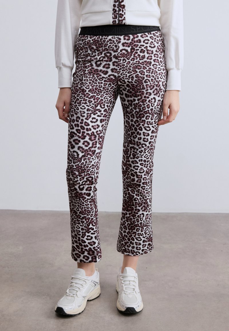 Παντελόνια με σχέδιο λεοπάρ σε μαλακό ύφασμα, με εφαρμοστή γραμμή και μαύρη αντίθετη μέση. Φοριούνται με λευκά αθλητικά παπούτσια.