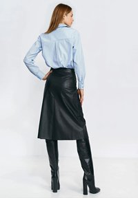 Jasnoniebieska koszula w paski zapinana na guziki, połączona z czarną skórzaną spódnicą midi i czarnymi, teksturowanymi kozakami sięgającymi do kolan, tworząca gładką sylwetkę.