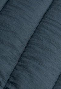 Gros plan sur un tissu matelassé bleu foncé avec des coutures visibles et une texture légèrement froissée.