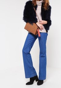 Navy umělá kožešinová bunda, béžový rolák, modré zvonové džíny, černé kotníčkové boty, hnědá crossbody taška s detailním třásněm.