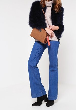 Giacca in ecopelliccia navy, dolcevita beige, jeans a zampa blu, stivaletti neri alla caviglia, borsa a tracolla marrone con dettaglio a frange.