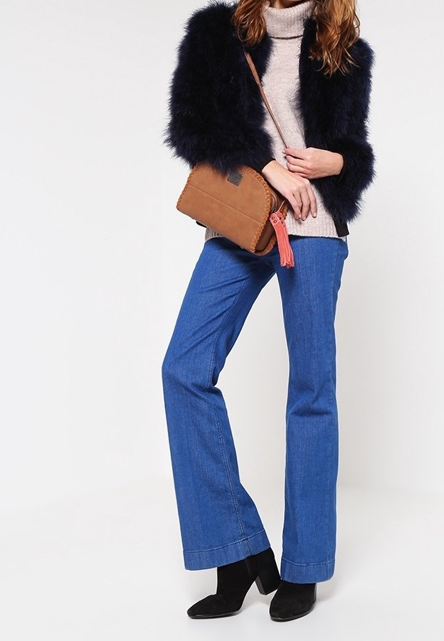 Navy umělá kožešinová bunda, béžový rolák, modré zvonové džíny, černé kotníčkové boty, hnědá crossbody taška s detailním třásněm.