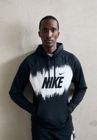 Svart og hvit Nike hettegenser med gradientmønster, stor logo på brystet, snorhette og glatt, elastisk stoff.